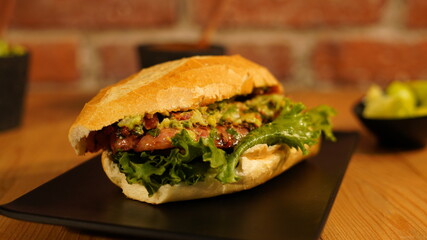 Choripan con chimichurri servido en un plato negro acompañado de salsa roja y verde, guacamole y limones