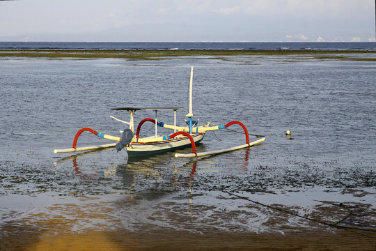 Jukung boat sitting on the sea floor during the low tide at Sanur Beach in Bali, Indonesia