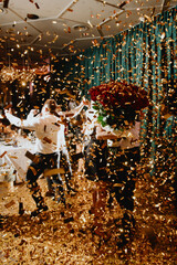 In a vibrant and lively atmosphere, a group of enthusiastic individuals are joyfully dancing in a room that is covered in shimmering gold confetti
