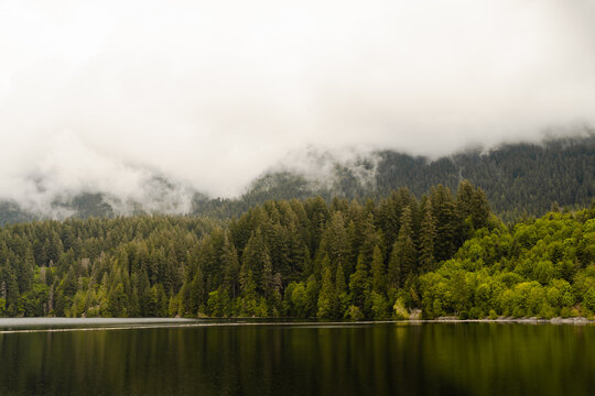 Front view of mountain in a cloud with pine trees and a lake