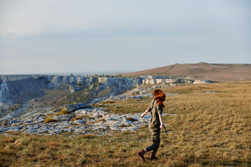 Naklejka premium Woman in hat enjoying a serene mountain view while walking through a grassy field in nature