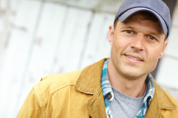 Man, farming and smile with cap in portrait by barn for job, agriculture and food production in countryside. Person, farmer and happy outdoor with pride for sustainable small business in Argentina