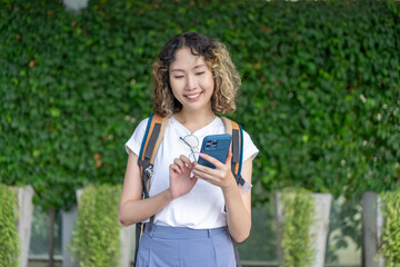 Asian cheerful young woman holding a smartphone, standing outdoors with a smile. Perfect for travel and lifestyle concepts.
