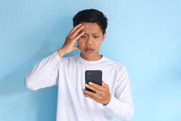 Young Asian man holding his mobile phone with sad expression 