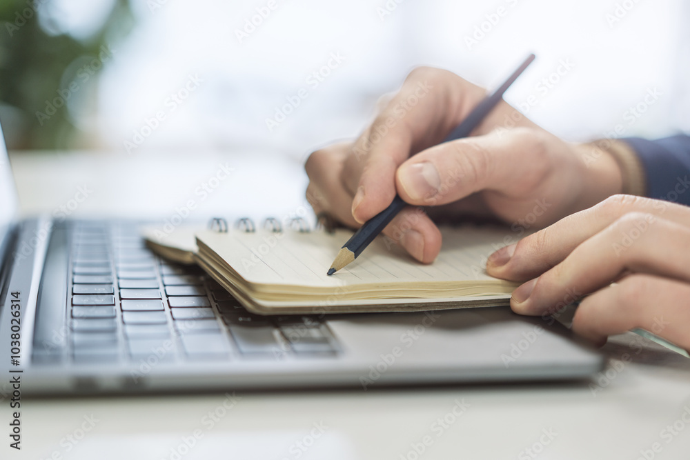 Aufkleber tight focus on a man's hand as he writes in a notepad on a contemporary laptop, background subtly bl