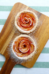 Pair of Mini Rose Shaped Apple Tartlets Sprinkled with Powdered Sugar on a Wooden Breadboard