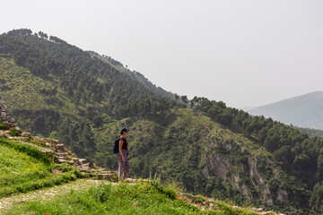 Tourist woman on colorful spring meadow overlooking idyllic town Berat seen from hilltop castle, Albania. Tranquil valles durrounded by majestic mountain Tomorr and rolling lush green hills. Tourism