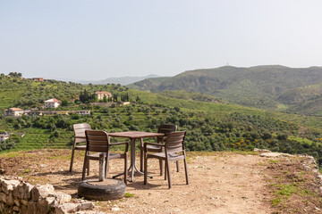 Small table and four chairs are set up on a gravel terrace, overlooking picturesque landscape in Berat, Albania, Europe. Peaceful outdoor dining area. Rolling hills, olive groves and mountain Tomorr