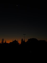 Dramatic sunset over the floodlights of Como Croquet Club with the moon visible in a cloudless sky, the orange glow the last of the daylight remaining on a perfect day in Western Australia.
