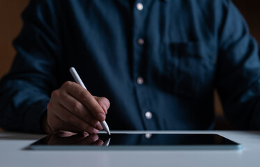 Man with pen in hand drawing or click on tablet lying on desk