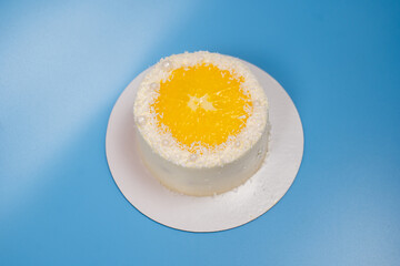Small coconut cake decorated with an orange slice and white pearls on blue background