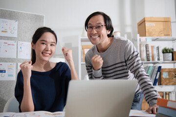 Two young Asian startup company entrepreneur partners brainstorm in casual small business office, marketing planning jobs on laptop, freelance work as E-commerce, happy and cheerful coworker team.