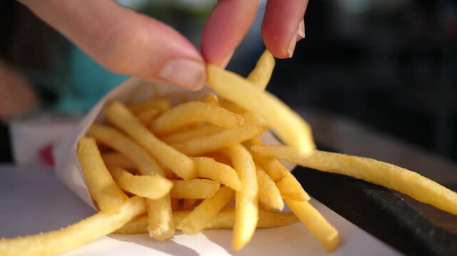 Closeup fingers picking up French fries potato chips from paper bag - eating in fast food restaurant