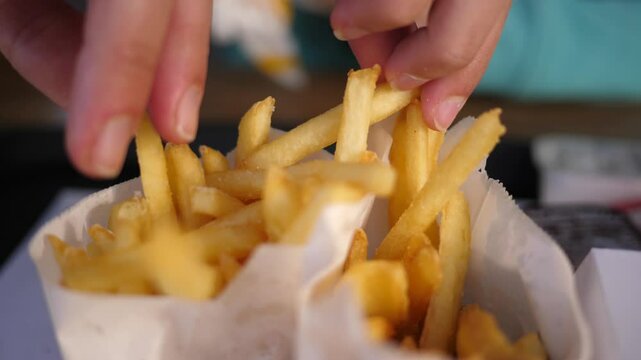Closeup fingers picking up French fries potato chips from paper bag - eating in fast food restaurant