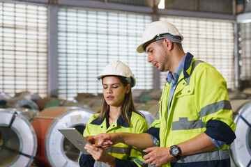 Workers in green uniforms and safety helmets perform quality checks inside a metal sheet factory.