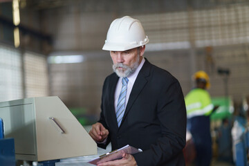 A man in a suit is looking at a computer screen while holding a clipboard to check product quality in the factory.