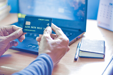 man's hand holding a fake credit card in front of a laptop, as an illustration of online shopping