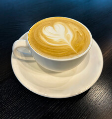Cappuccino coffee in the white cup on the black wooden background. Top view. Close-up.