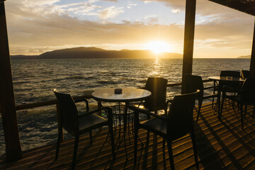 Sunset over mountains. Sea landscape. Restaurant terrace by the sea. Table and chairs with a perfect view. Café sunset view. Place for watching the sunset. Romantic atmosphere and a serene location.