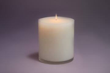 An isolated beautiful white candle burns on a purple background, in the center. Flame of hope