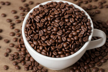 Obraz premium A white cup filled with coffee beans and coffee beans scattered on a wooden surface