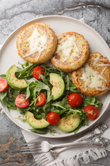 Eggy cheese crumpets with vegetables salad closeup on the plate on the table. Vertical top view from above