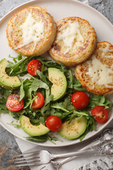 Delicious hot egg cheese crumpets with fresh vegetable salad close-up in a plate on the table. Vertical top view from above