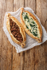 Turkish Pide Flat Bread Filled with ground beef, Cheese, Spinach and Herbs close-up on wooden board on table. Vertical top view from above