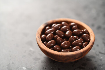 Milk chocolate dragee in olive wood bowl on concrete background