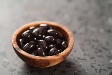 Obraz premium Dark chocolate dragee in olive wood bowl on concrete background