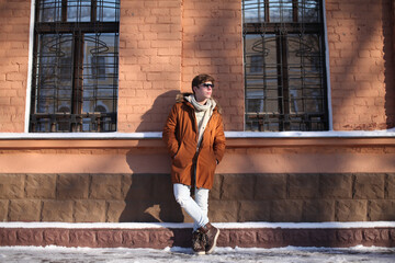 Stylish young man full-length looking away wearing jacket standing against wall on a city street