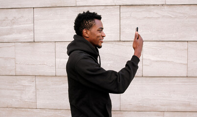 Stylish happy African young man taking selfie with phone, black american guy smile using smartphone