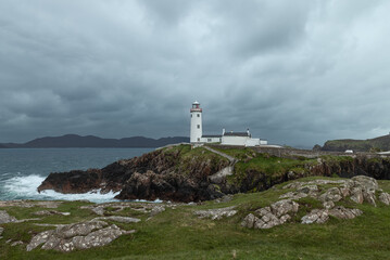 Panoramic view of Fanad Head Lighthouse surrounded by stormy skies, rugged cliffs, and crashing waves, capturing the wild Irish coastline