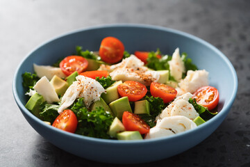 Salad with avocado, mozzarella, tomatoes and kale in blue ceramic bowl