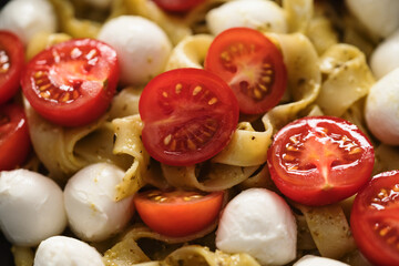 fettuccine pasta with pesto, mozzarella and cherry tomatoes in black bowl closeup