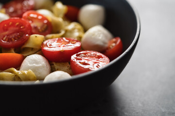 fettuccine pasta with pesto, mozzarella and cherry tomatoes in black bowl on concrete background closeup with copy space