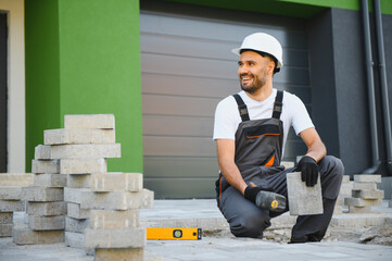 The master in gloves lays paving stones in layers. Garden brick pathway paving by professional...