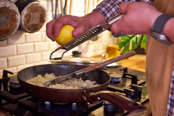 a man rubs lemon zest in a skillet of vegetables