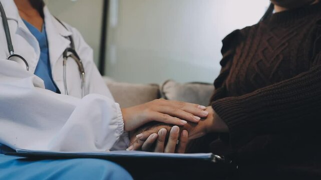 Doctor giving hope. Close up shot of young female physician leaning forward to smiling elderly lady patient holding her hand in palms. Woman caretaker in white coat supporting encouraging old person