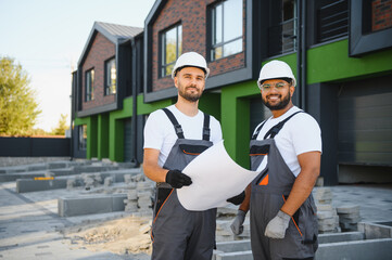 Two builders or architects checking the construction plan against the background of new cottages