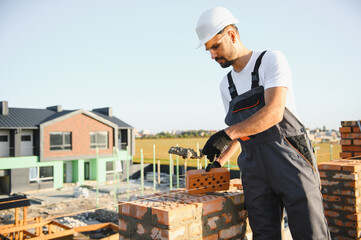 construction mason worker bricklayer installing red brick with trowel putty knife outdoors