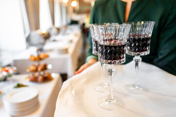 crystal wine glasses filled with red wine, held by a person in a green garment. background features blurred banquet setting, creating a warm and elegant atmosphere. Perfect for celebrations and events