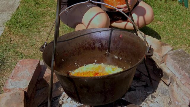 A traditional Romanian cooking scene showing onions being saut&eacute;ed in a cauldron over a wood fire, a key step in making authentic zacusca. The rustic outdoor setup highlights the time-honored methods.