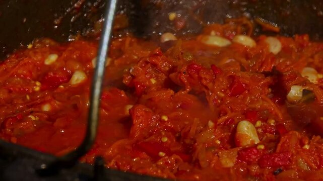 A traditional Romanian cooking moment where tomato puree is poured into a cauldron over a wood fire. This rustic outdoor scene captures the making of authentic zacusca, a flavorful spread