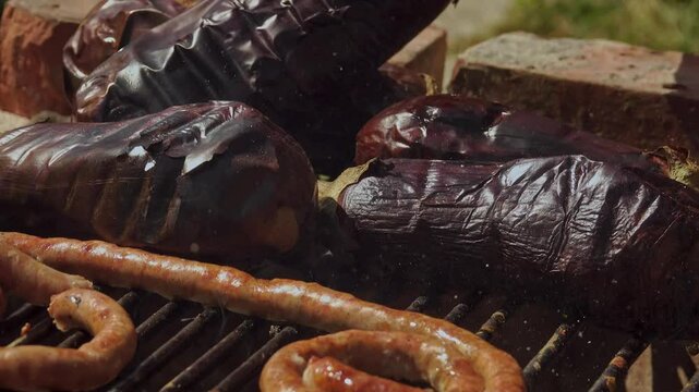 A rustic outdoor scene of vegetables grilling over a wood fire, an essential step in making traditional Romanian zacusca. The fire-roasted vegetables bring out deep, smoky flavors