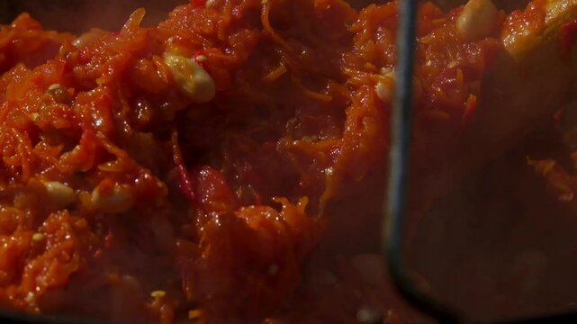 A traditional Romanian cooking moment where tomato puree is poured into a cauldron over a wood fire. This rustic outdoor scene captures the making of authentic zacusca, a flavorful spread