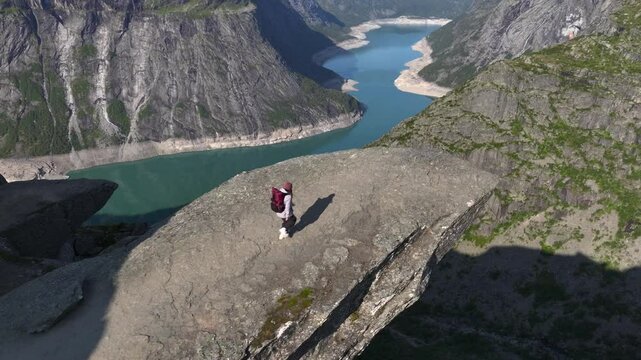 Girl with Backpack on the edge of cliff on Trolltunga, Norway. Aerial of Norwegiant Highlight SIghtseeing Troll Tongue