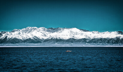 A lone boat sailing in the Sayram Lake (Sailimu Hu) in front of snow-capped mountains in Xinjiang, China