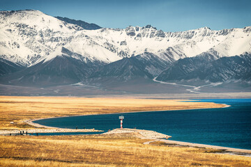 A lone lighthouse standing on the S-shaped coastline of Sayram Lake (Sailimu Hu) with snow-capped mountains in the distance in Xinjiang, China