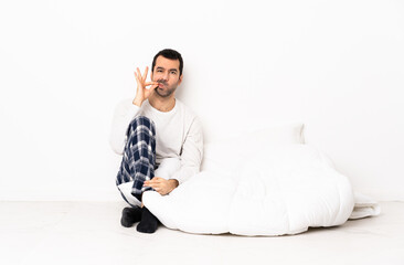 Caucasian man in pajamas sitting on the floor at indoors showing a sign of silence gesture